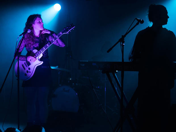 Connor Moore performing with electric guitar on stage lit with blue and purple